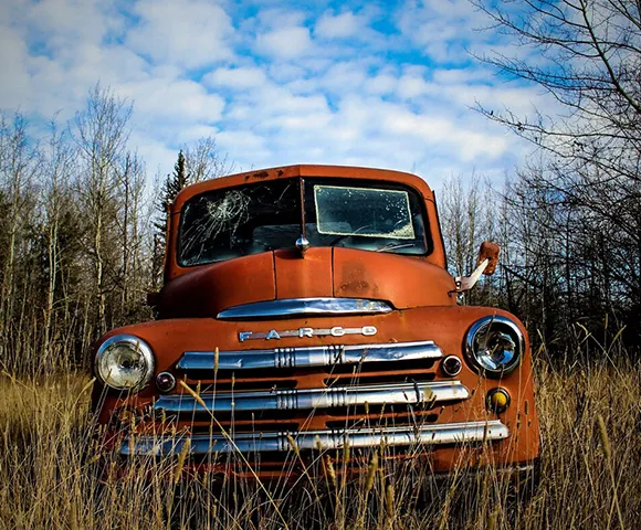 Rusty orange vintage truck parked outdoors under blue sky.