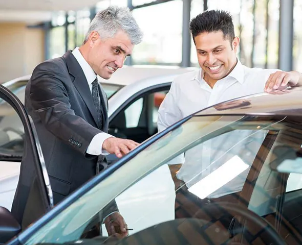Car salesmen and customer reviewing vehicle details for car selling service in Irving, TX