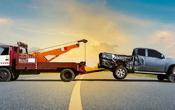 Tow truck hauling damaged black car on highway for junk car removal service.