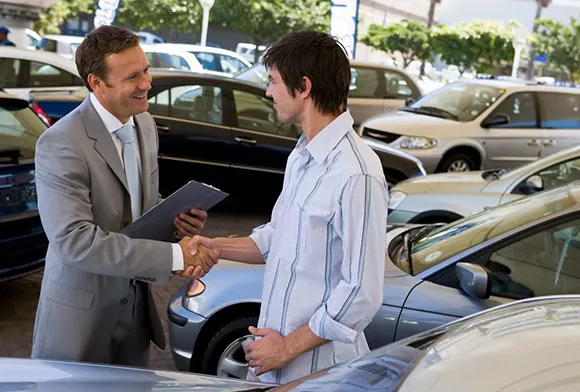Car buyer and seller shaking hands at dealership for fast car sale process.