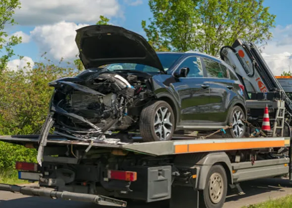 Black car with open hood loaded on flatbed tow truck for junk car pickup in Carleton, TX