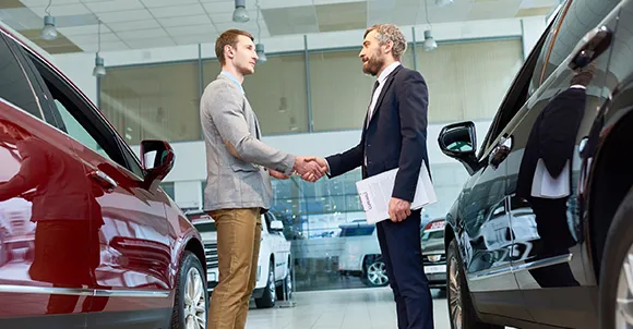 Two men shaking hands in a car dealership with cars parked around, symbolizing quick car sales in Arlington, TX.