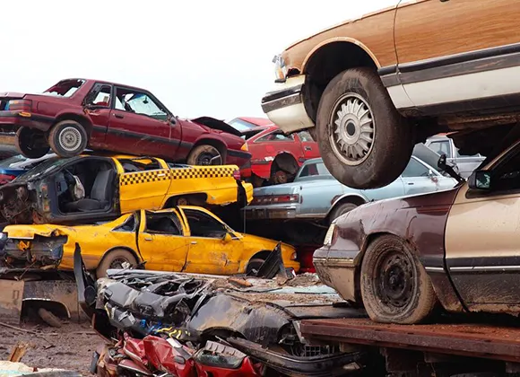 Stacked scrap cars in junkyard with car being lifted for scrap removal service in Carleton, TX
