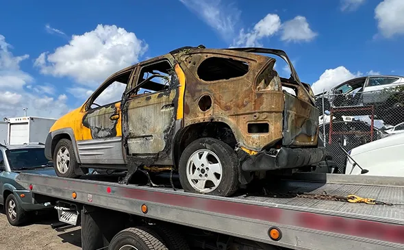 Burnt damaged car on flatbed tow truck for same day junk car pickup in Irving, TX