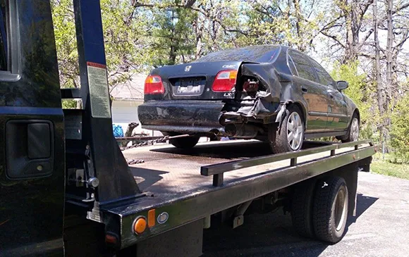 Black car loaded on flatbed tow truck for same day junk car pickup in Plano, TX
