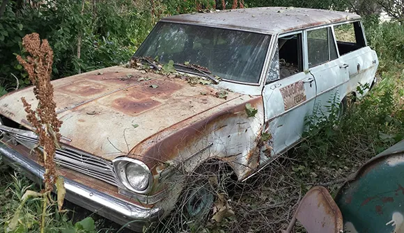 Rusty green vintage car overgrown with weeds awaiting junk car removal in Rockwall, TX